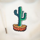 A close up of an embroidered cactus on a natural off white hoodie 