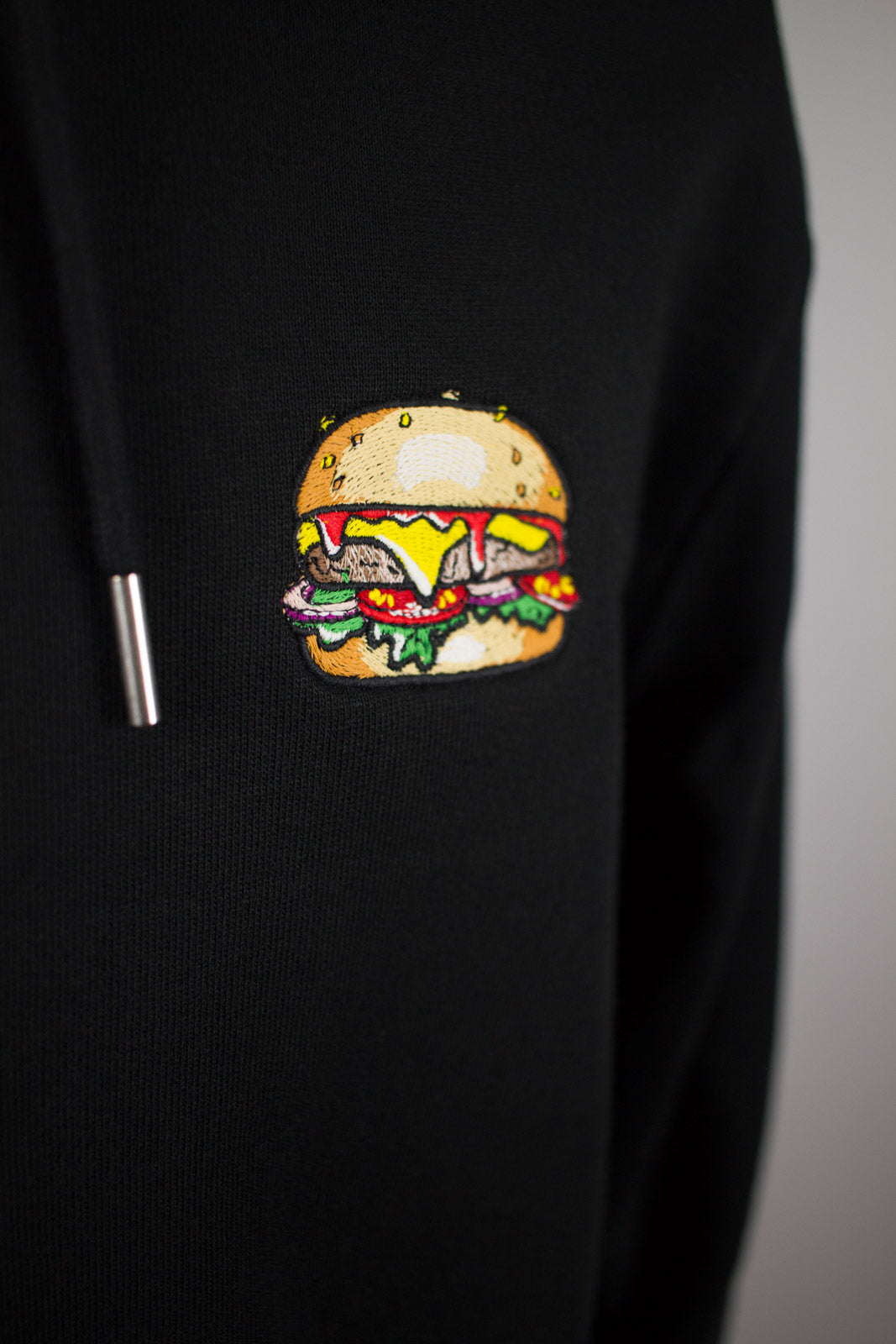 Close up of embroidered burger design on a black Hoodie by The Embroidery Crew