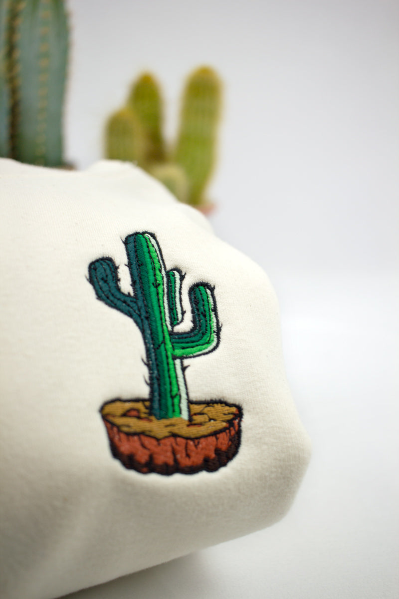 A close up of an embroidered cactus on a natural off white hoodie